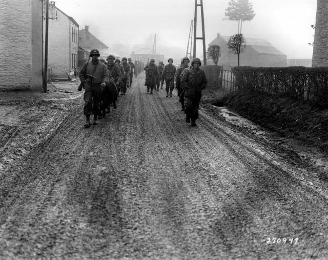 Men of the 28th Infantry Division march down a street in Bastogne, Belgium, December 1944. Some of these men lost their weapons during the German advance in this area.