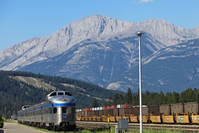 A Via Rail passenger train passes by freight trains in the background, in Jasper station