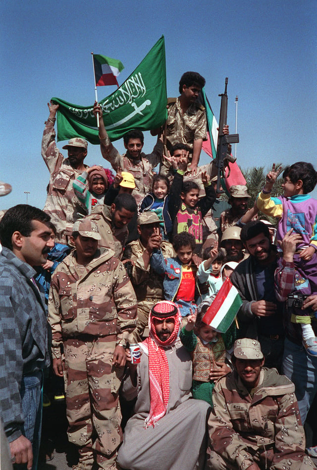Civilians and coalition military forces wave Kuwaiti and Saudi Arabian flags as they celebrate the retreat of Iraqi forces from Kuwait