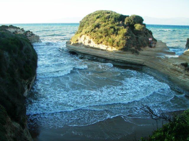 The famous beach at Canal D'Amour, Sidari on a windy day. At the entrance of the bay there is an opening in the rock at the right (centre left of picture) that continues to the other side, a natural tunnel. This sea channel gave the beach its name: Canal D'Amour, French for channel of love.