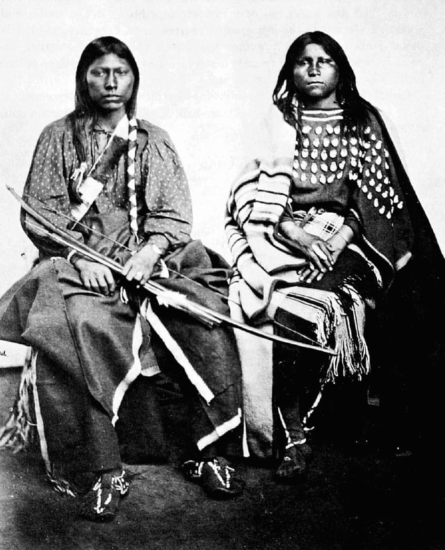 A Kiowa couple. The woman on the right is wearing an elk tooth dress.