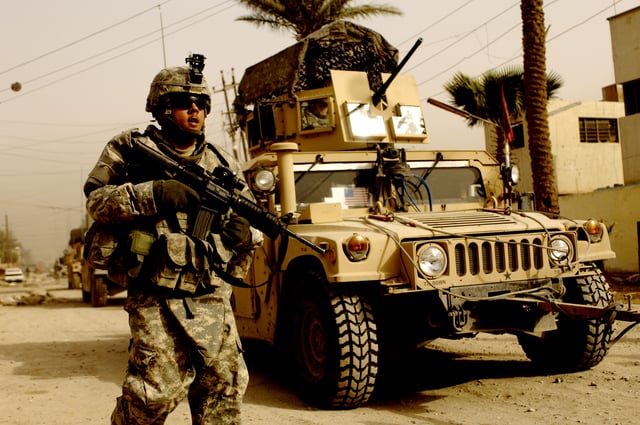 A U.S. soldier on patrol with the support of a Humvee vehicle
