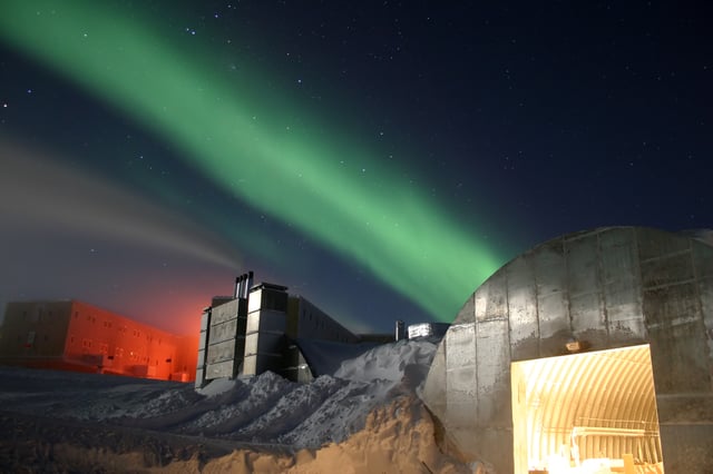 A full moon and 25-second exposure allowed sufficient light for this photo to be taken at Amundsen–Scott South Pole Station during the long Antarctic night. The station can be seen at far left, the power plant in the centre and the mechanic's garage in the lower right. The green light in the background is the aurora.