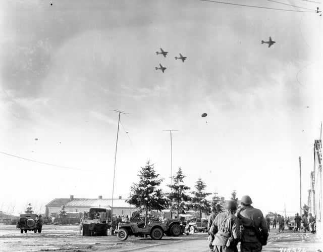 101st Airborne Division troops watch as C-47s drop supplies over Bastogne.