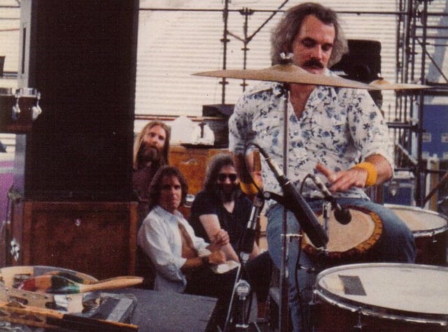 Grateful Dead members in the early 1980s: Brent Mydland, Bob Weir, and Jerry Garcia watch Bill Kreutzmann play the drums. Not pictured are Phil Lesh and Mickey Hart.