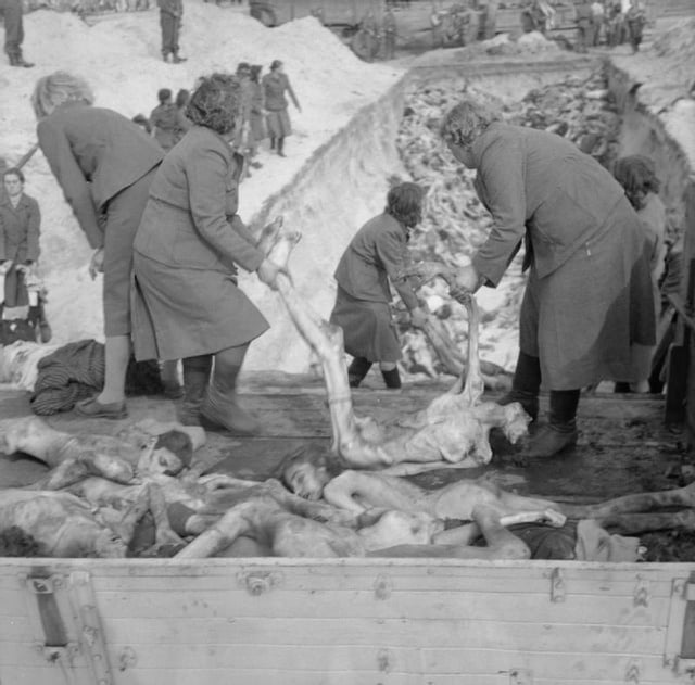 Schutzstaffel (SS) female camp guards removing prisoners' bodies from lorries and carrying them to a mass grave, inside the German Bergen-Belsen concentration camp, 1945