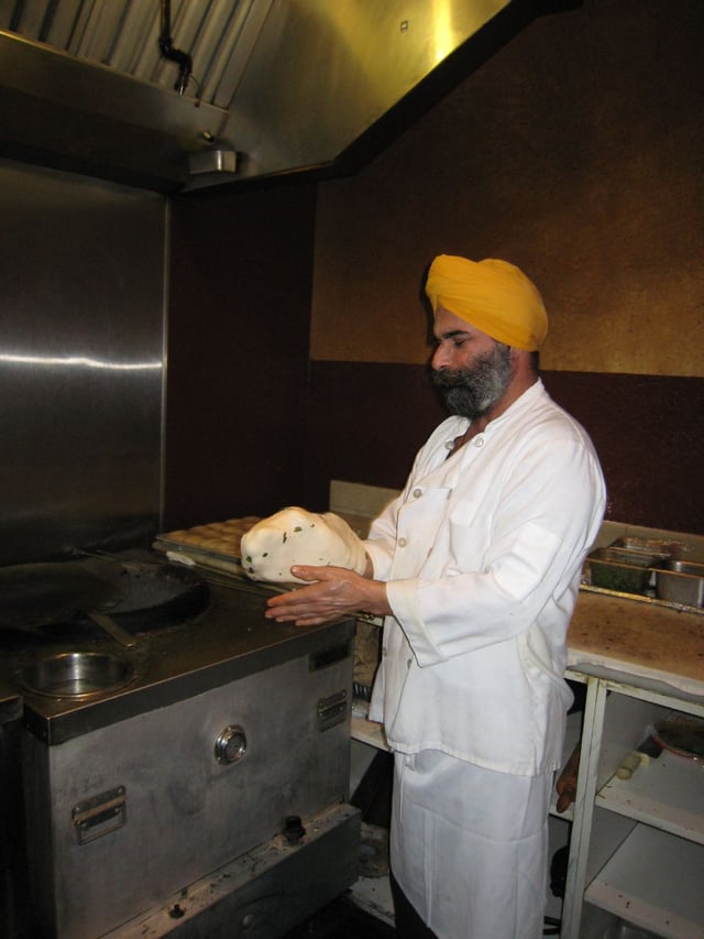 Chef preparing naan to be cooked in a tandoor.