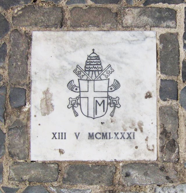 Small marble tablet in St. Peter's Square indicating where the shooting of John Paul II occurred. The tablet bears John Paul's personal papal arms and the date of the shooting in Roman numerals.