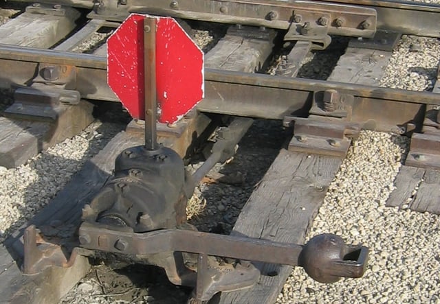 An example of a mechanism used at a switch. The two points are linked together with a throw bar. The throw bar extends to the lever on the near side of the track, which is used to throw the switch. This is an example of a low switch stand, used at locations where there is not sufficient clearance for a tall switch stand. This particular stand is designed to be trailed through by rolling stock, which will cause the points to become lined for the route that the wheels have passed through. It has a reflectorised target.