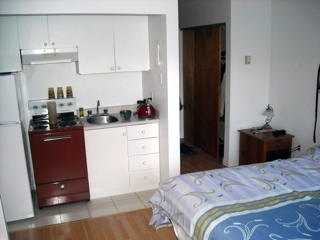 Studio apartment in Sherbrooke, Quebec, Canada, showing double bed, kitchenette, and entrance way with sliding door to closet