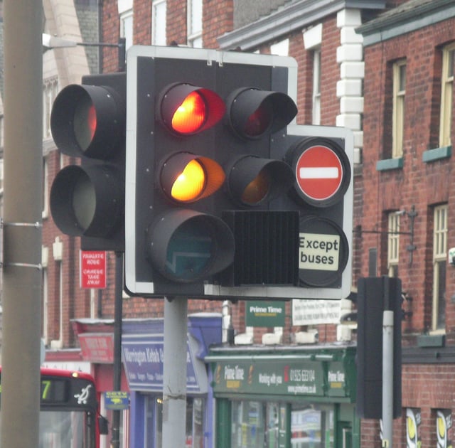 Traffic lights can have several additional lights for filter turns or bus lanes. This one in Warrington, United Kingdom, also shows the red + orange combination seen in a number of European countries, and a backing board with white border to increase the target value of the signal head. Improved visibility of the signal head is achieved during the night by using the retro-reflective white border.