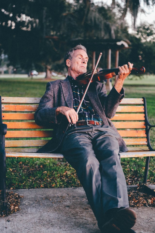 Man playing violin on a park bench.