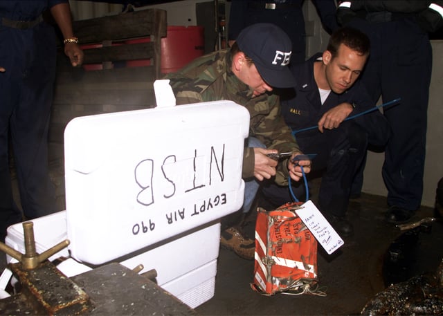 An FBI agent tags the cockpit voice recorder from EgyptAir Flight 990 on the deck of the USS Grapple (ARS 53)
