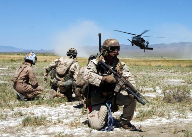 Pararescuemen and a simulated "survivor" watch as an HH-60G Pave Hawk helicopter comes in for a landing.