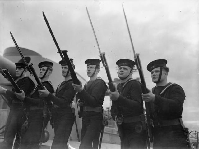 Six sailors with Lee–Enfield rifles, standing in the 'On Guard' position during rifle and bayonet drill on board the Battleship HMS RODNEY.