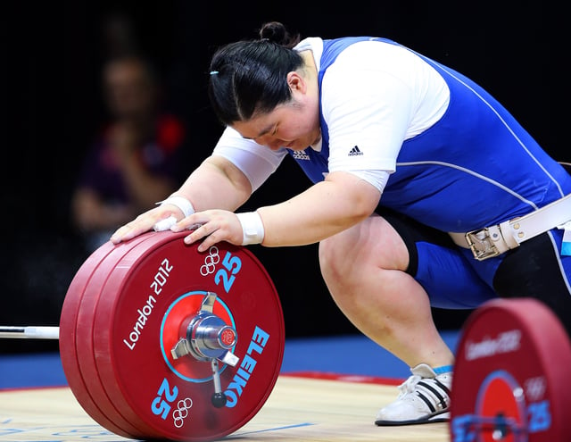 An Olympic lifter, Jang Mi-ran, holding a barbell loaded with red 25 kg bumper plates, held in place with a collar. Note the lifter's taped wrists and thumbs, her weightlifting shoes, and her weightlifting belt.