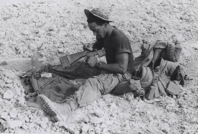 Sitting in the middle of a virtual dustbowl on Go Noi Island, a Marine pauses to clean his M16 rifle, Operation Pipestone Canyon, Vietnam, 1969