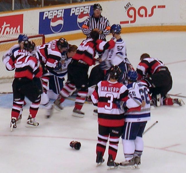 Altercations often occur near the goal after a stoppage of play, since defensive players are highly concerned with protecting their goaltender, seen here in a match between Ottawa and Sudbury of the Ontario Hockey League.
