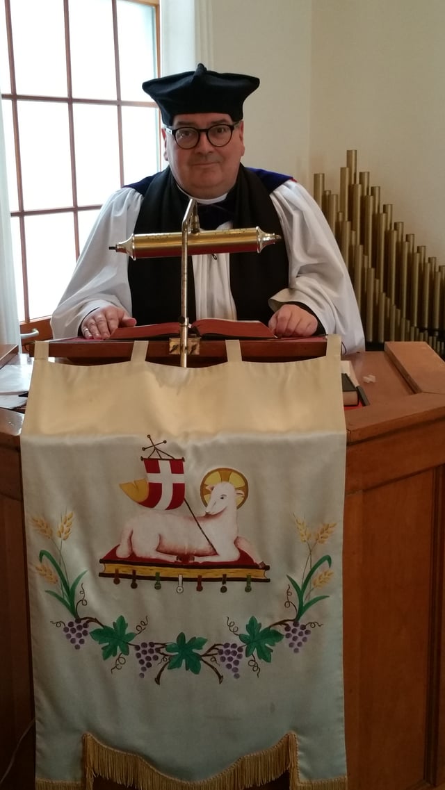 An Anglican minister delivers a homily, dressed in choir habit with Canterbury cap