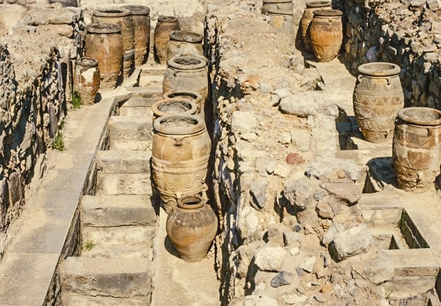 Magazine 4 with giant pithoi placed by the archaeologists for display. The compartments in the floor were the permanent locations of pithoi, or storage jars, such as these, which stored wet and dry consumables, such as wine, oil, and grain. When full, they were multi-ton and immoveable. They were sunken for easier access to the wide mouths and for support.