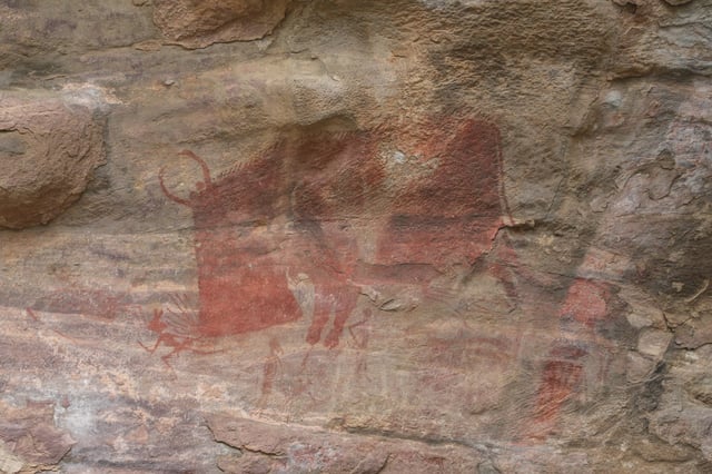 Mesolithic rock art at the Bhimbetka rock shelters, Madhya Pradesh, showing a wild animal, perhaps a mythical one, attacking human hunters.  Although the rock art has not been directly dated, it has been argued on circumstantial grounds that many paintings were completed by 8000 BCE, and some slightly earlier.
