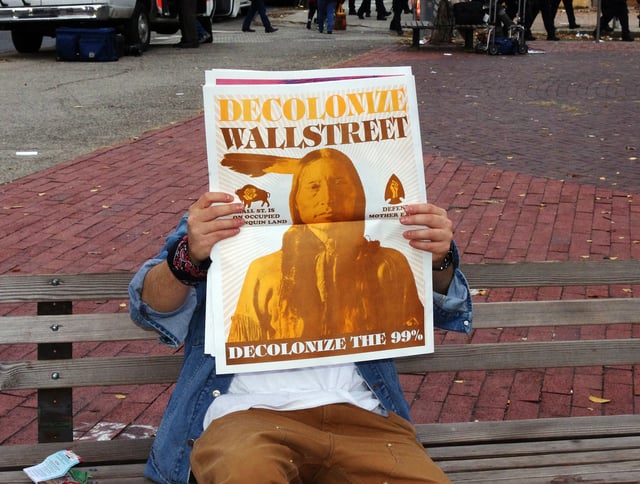 Occupier reading the special edition of Occupied Wall Street, with posters curated by Occuprint.