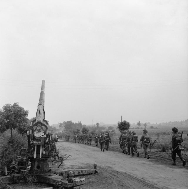 Infantry of 50th (Northumbrian) Division moving up past a knocked-out German 88mm gun near 'Joe's Bridge' over the Meuse-Escaut Canal in Belgium, 16 September 1944