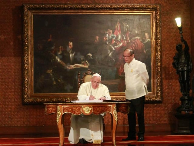 President Benigno Aquino III witnesses as Pope Francis signs the Palace Guestbook, the 'Blood Compact' painting in the background.