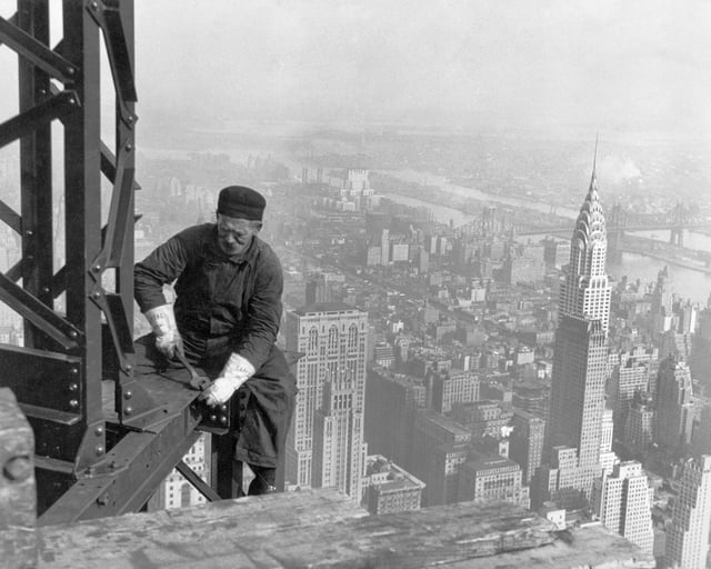 A worker bolts beams during construction; the Chrysler Building can be seen in the background.