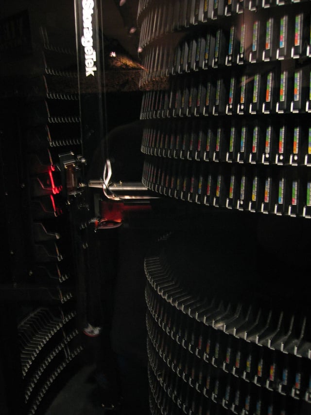 A large tape library, with tape cartridges placed on shelves in the front, and a robotic arm moving in the back. Visible height of the library is about 180 cm.