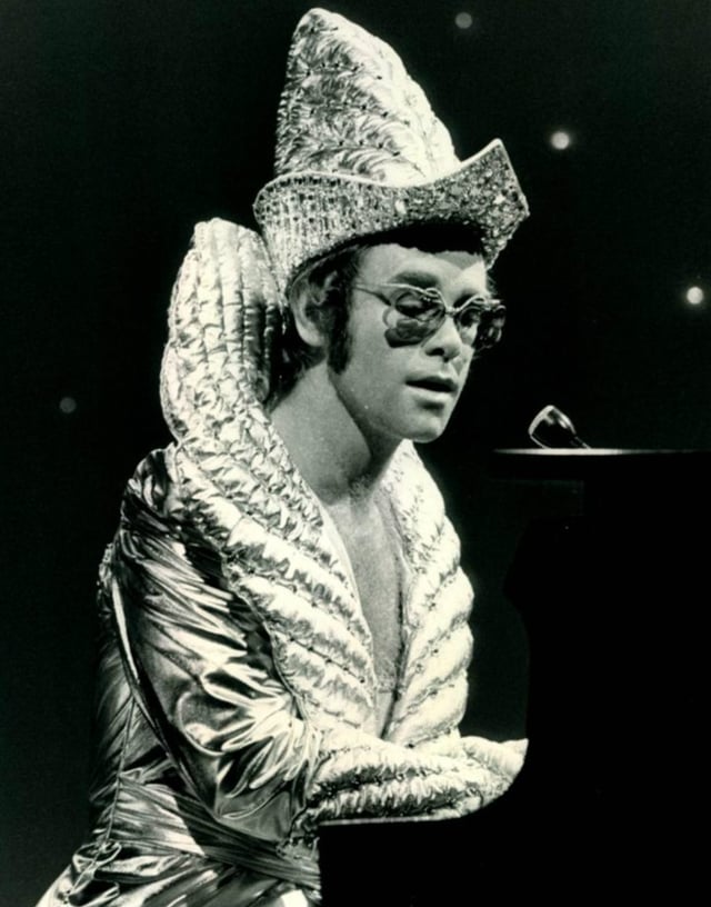 Elton John often wore elaborate stage costumes as part of the glam rock era in the UK music scene.