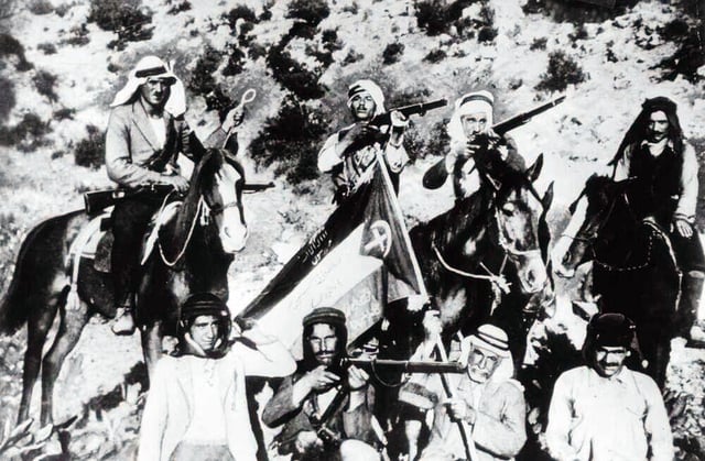 Rebels, some mounted on horses, posing with their rifles and a Palestinian flag emblazoned with a cross and crescent, 1937