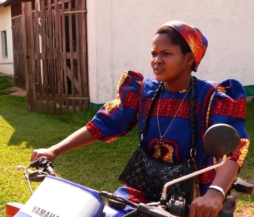A sister of the Theresienne Sisters of Basankusu wearing a brightly coloured habit, riding a motor-bike, Democratic Republic of Congo, 2013