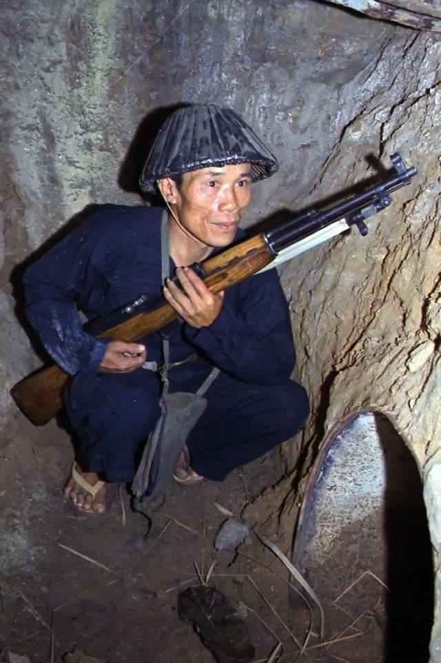 A guerilla of the People's Liberation Armed Forces of South Vietnam, crouching in an underground tunnel, holding an SKS carbine.