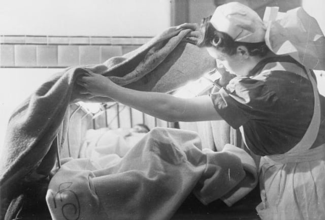 In London Hospital, England, 1941, nurse arranges an asbestos blanket over an electrically heated frame to create a hood over this patient to help warm them quickly