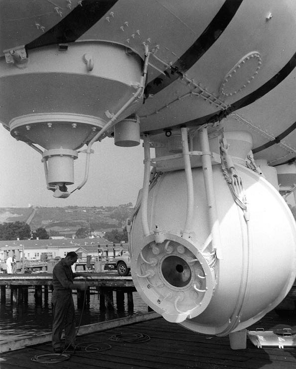 Close-up of pressure sphere of Bathyscaphe Trieste, with a single conical window of PMMA (Plexiglas) set into sphere hull. The very small black circle (smaller than the man's head) is the inner side of the plastic "window," and is only a few inches in diameter. The larger circular clear black area represents the larger outer-side of the thick one-piece plastic cone "window."