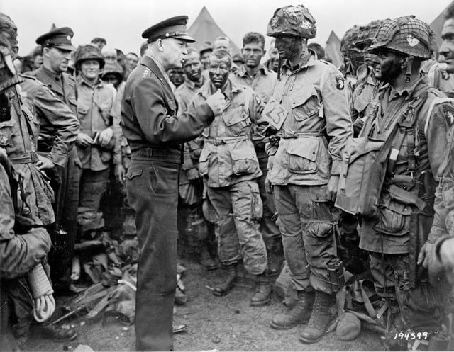General Dwight D. Eisenhower speaking with 1st Lieutenant Wallace C. Strobel and men of Company E, 502nd Parachute Infantry Regiment on 5 June. The placard around Strobel's neck indicates he is the jumpmaster for chalk No. 23 of the 438th TCG.