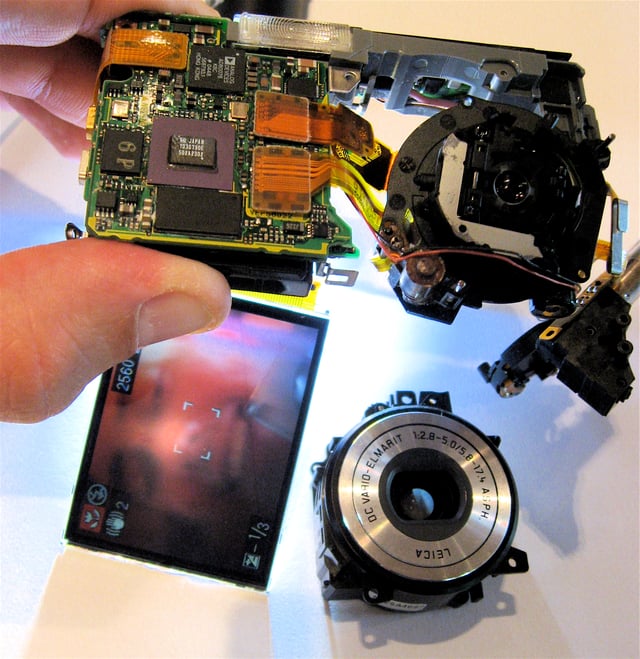 Digital camera, partly disassembled. The lens assembly (bottom right) is partially removed, but the sensor (top right) still captures an image, as seen on the LCD screen (bottom left).