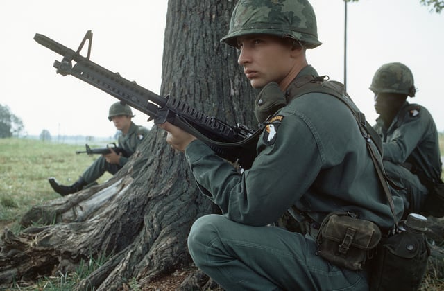 A member of the 101st Airborne Division, armed with an M60 machine gun, participates in a field exercise in 1972. M16A1 rifle in background with each soldier wearing an M1 helmet.