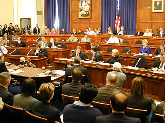 The House Financial Services committee meets. Committee members sit in the tiers of raised chairs, while those testifying and audience members sit below.
