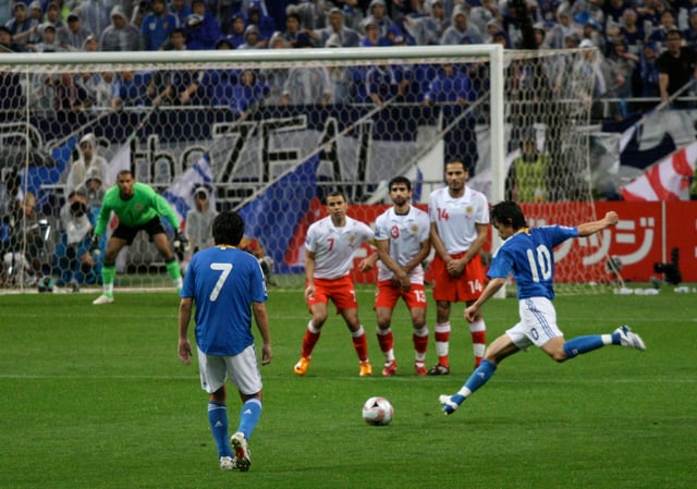 A player takes a free kick, while the opposition form a "wall" to try to block the ball