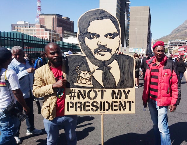A protest placard depicting Atul Gupta carried by two EFF members at a Zuma Must Fall protest in Cape Town, 2017