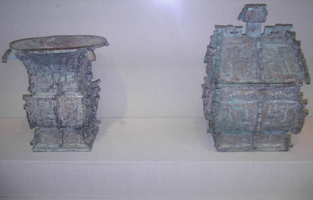 Left: Bronze fāngzūn (方樽) ritual wine container dated about 1000 BC. The inscription cast in bronze on the vessel commemorates a gift of cowrie shells (then used as currency in China) from someone of presumably elite status in Zhou dynasty society. Right: Bronze fāngyí (方彝) ritual container dated about 1000 BC. An inscription of some 180 Chinese characters appears twice on the vessel. The inscription comments on state rituals that accompanied court ceremony, recorded by an official scribe.