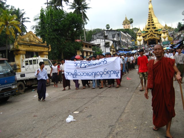 Protesters in Yangon during the 2007 Saffron Revolution with a banner that reads non-violence: national movement in Burmese. In the background is Shwedagon Pagoda.