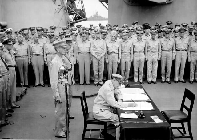 MacArthur signs the Japanese Instrument of Surrender aboard the USS Missouri. American General Jonathan Wainwright and British General Arthur Percival stand behind him.