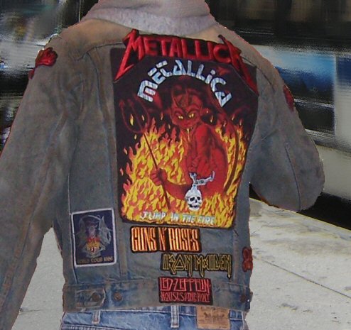 A heavy metal fan wearing a denim jacket with band patches and artwork of the heavy metal bands Metallica, Guns N' Roses, Iron Maiden, Slipknot, Dio and Led Zeppelin.