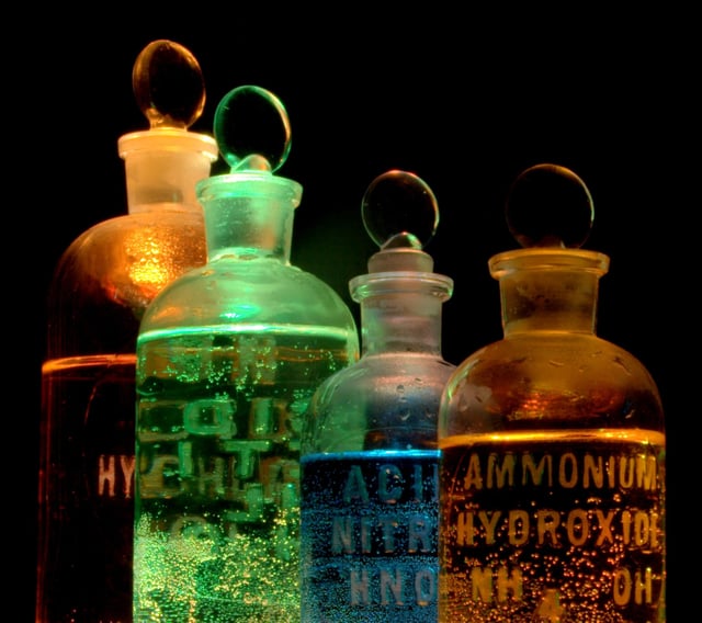 Solutions of substances in reagent bottles, including ammonium hydroxide and nitric acid, illuminated in different colors