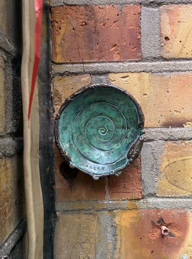 A bronze work by Jonesy on a wall in Brick Lane (London). Diameter about 8 cm.
