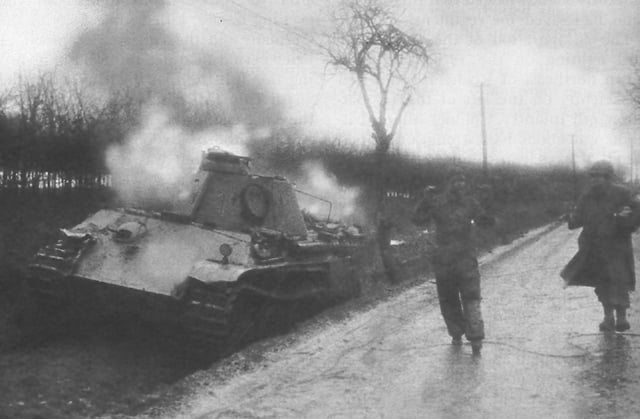 An American soldier escorts a German crewman from his wrecked Panther tank during the Battle of Elsenborn Ridge.