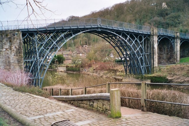 The cast iron Iron Bridge at Coalbrookdale, opened in January 1781 and was the first large-scale object made out of cast iron; but cast iron is not reliably strong due to impurities. Wrought iron, where the carbon is hammered to remove to carbon and impurities is much stronger; the first large-scale wrought iron bridge was the Britannia Bridge over the Menai Strait, only possible due to its innovative box girder design by Robert Stephenson